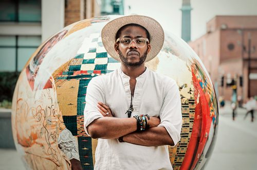 artist Àsìkò standing in front of globe-shaped art piece